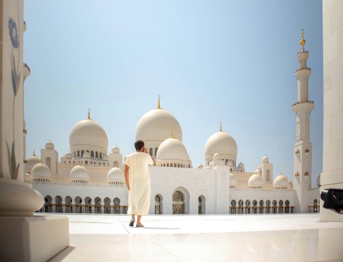 Man in white standing outside Sheikh Zayed Grand Mosque against a blue sky