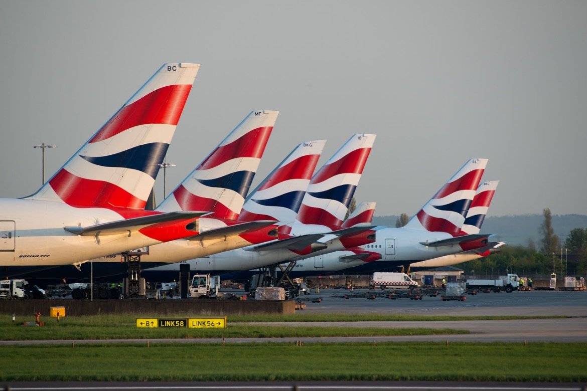 7 British Airways aircraft tails lined up on a runway. 