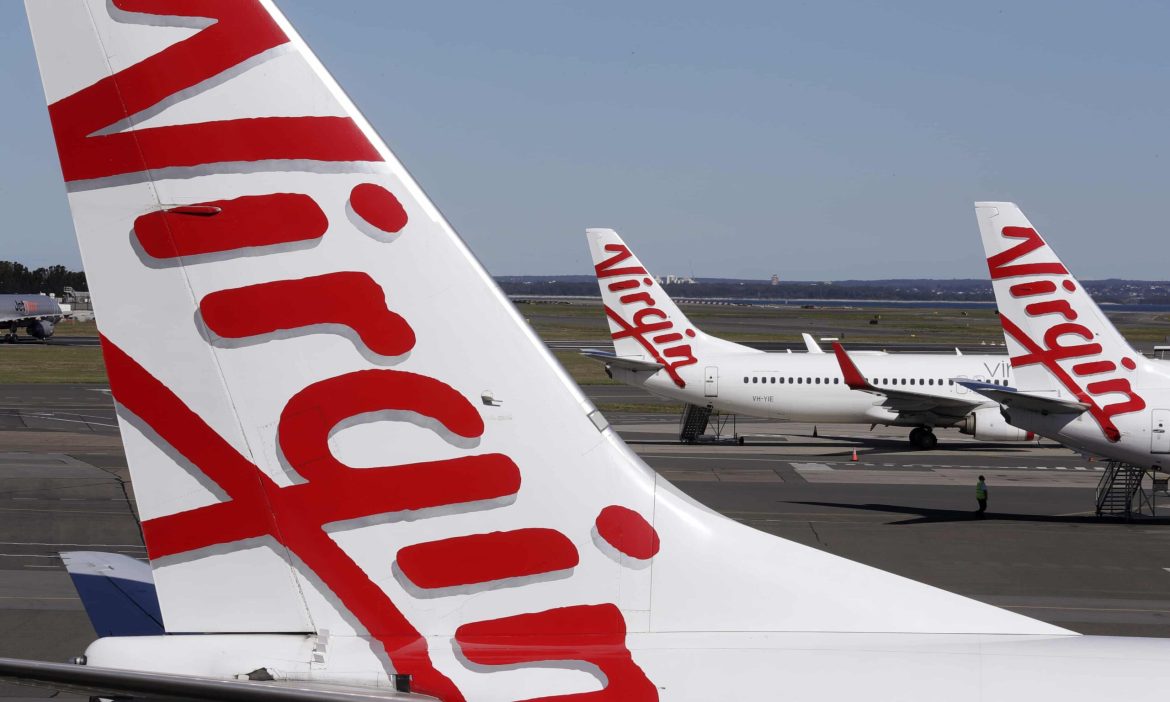 Three Virgin Australia plane’s are parked on a runway, one of the planes tails being the main focus of the image.