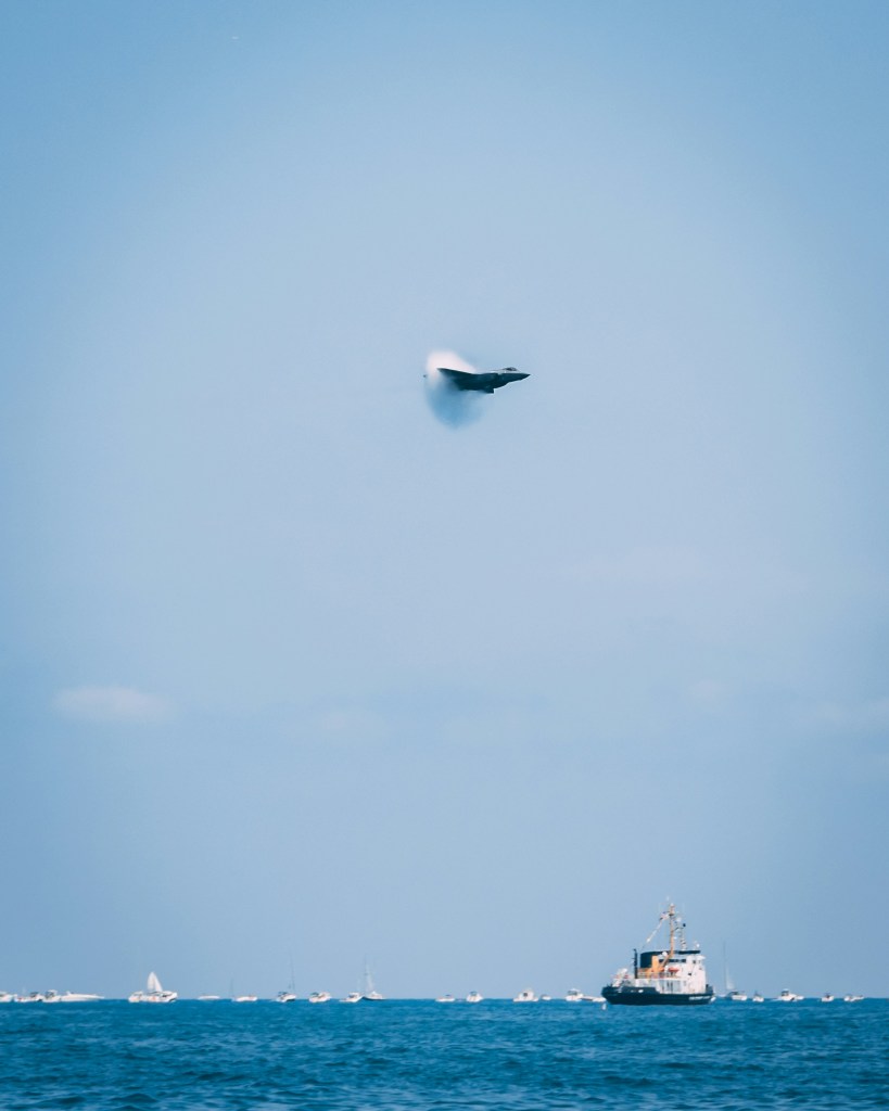 A supersonic jet breaking the sound barrier over a boat. 