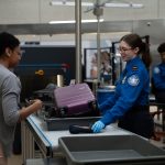 A TSA officer checks a passenger's carry-on baggage