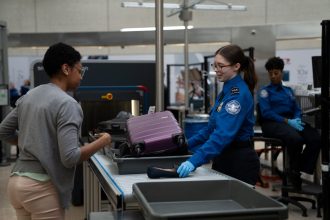 A TSA officer checks a passenger's carry-on baggage